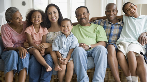 A multi-generational family sits together on a coach